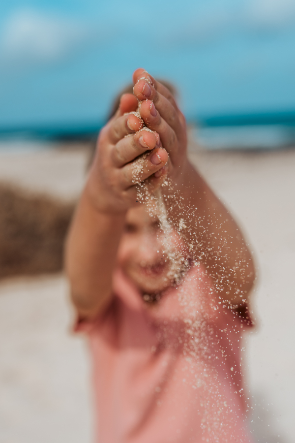 Girl with sand falling from her palms standing on beach. Family summer vacation by the sea.