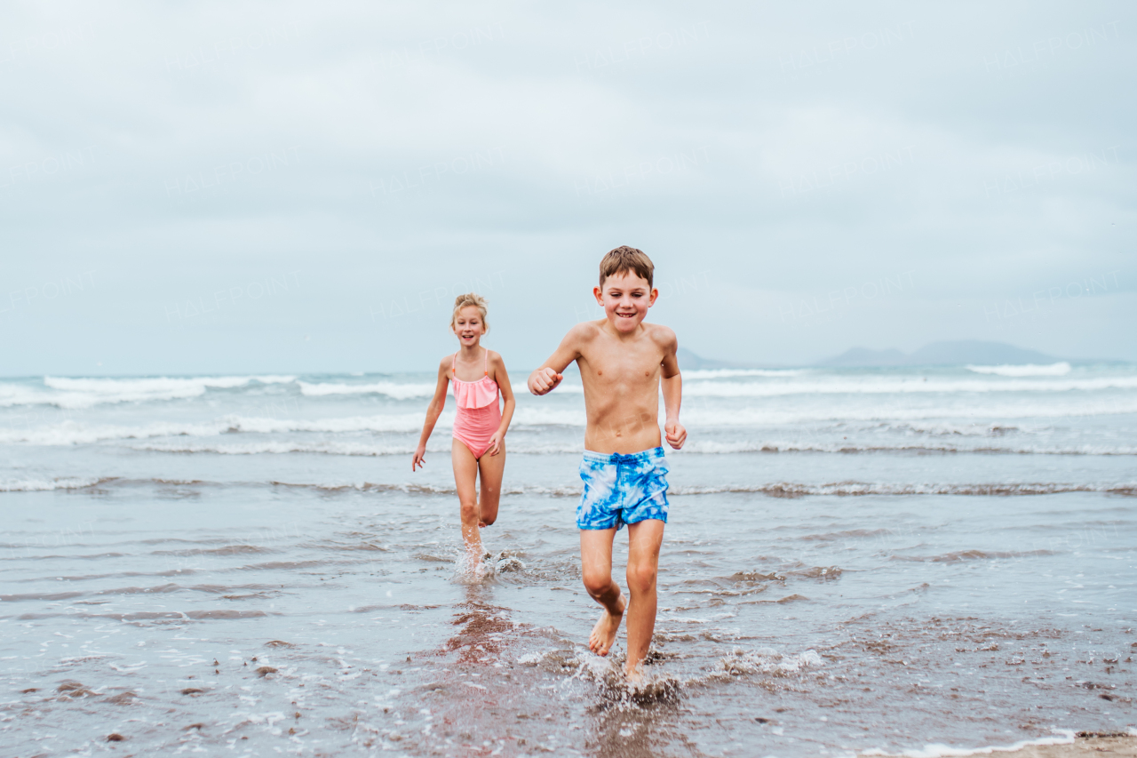 Siblings playing on beach, running, having fun. Smilling girl and boy on sandy beach of Canary islands. Concept of a family beach summer vacation with kids.