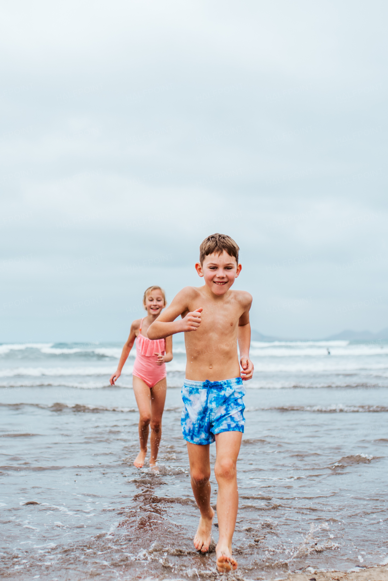 Siblings playing on beach, running, having fun. Smilling girl and boy ion sandy beach with vulcanic rocks of Canary islands. Concept of a family beach summer vacation with kids.