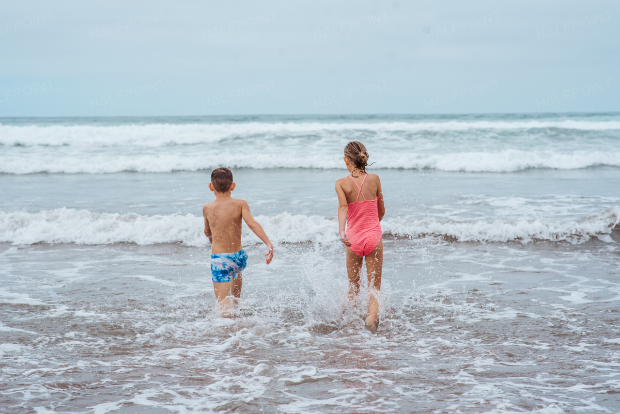 Siblings playing on beach, running, skipping and having fun on sandy beach of Canary islands. Concept of family beach summer vacation with kids.