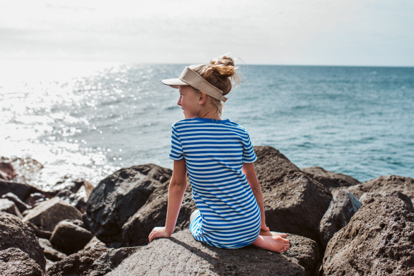 Rear view of beautiful girl by sea. Blonde girl in striped dress enjoying vacation in Canary Islands. Concept of beach summer vacation with kids.