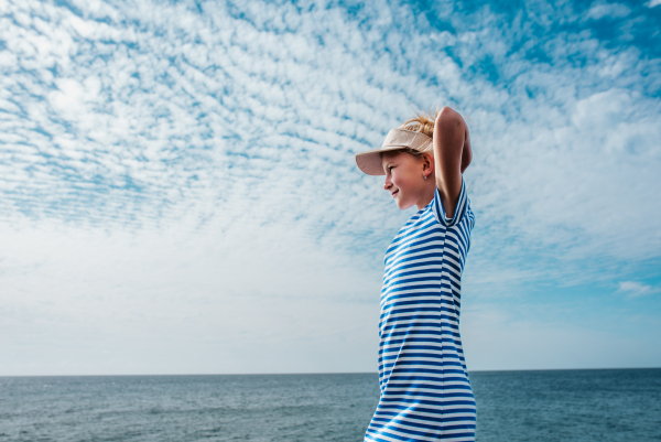 Side view of beautiful girl by sea. Blonde girl in striped dress enjoying vacation in Canary Islands. Concept of beach summer vacation with kids.