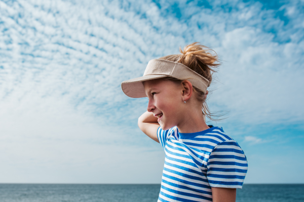 Side view of beautiful girl by sea. Blonde girl in striped dress enjoying vacation in Canary Islands. Concept of beach summer vacation with kids.