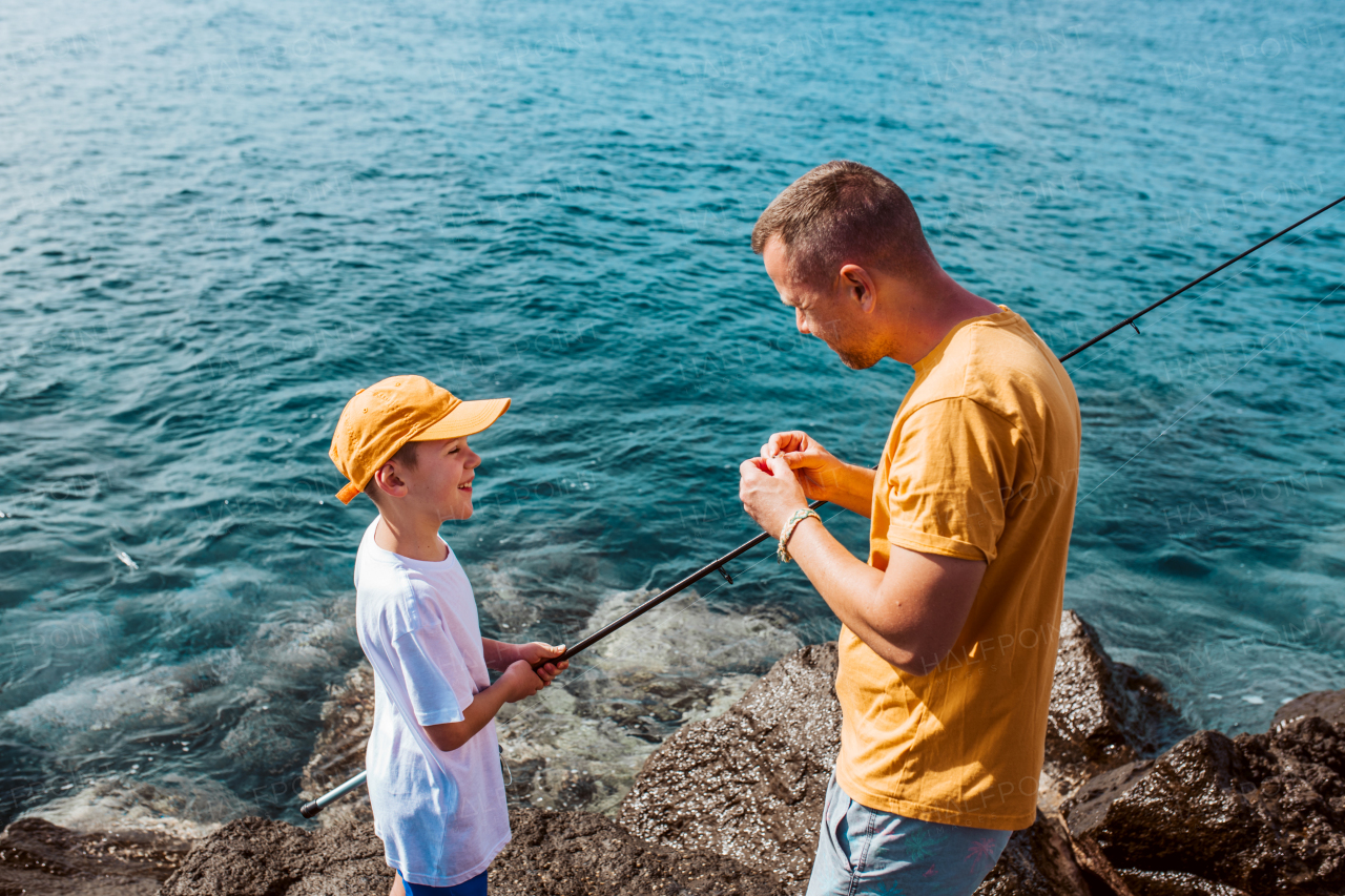 Father teaching young son fishing in the sea. Standing on rock, coast together holding fish rod. Top view of dad and boy.