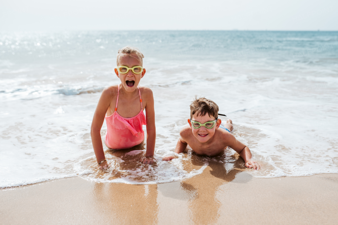 Siblings playing on beach, running, having fun. Smilling girl and boy on sandy beach with vulcanic rocks of Canary islands. Concept of a family beach summer vacation with kids.