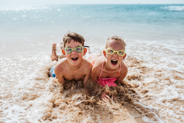 Siblings playing on beach, running, having fun. Smilling girl and boy on sandy beach with vulcanic rocks of Canary islands. Concept of a family beach summer vacation with kids.