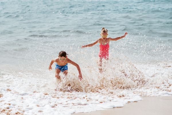 Siblings playing on beach, running, having fun. Smilling girl and boy on sandy beach with vulcanic rocks of Canary islands. Concept of a family beach summer vacation with kids.