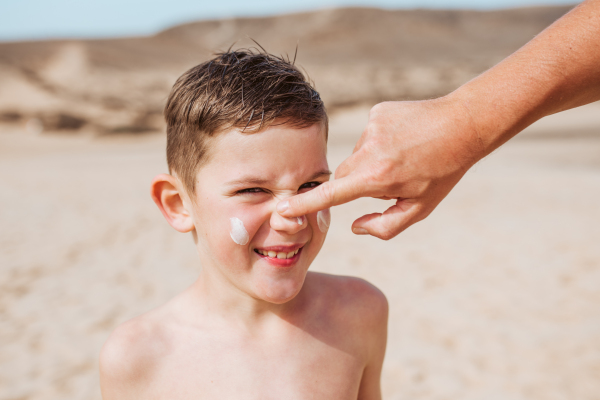 Boy with sunscreen lotion on face. Young boy si protected from sun with sunscreen. Concept of family beach summer vacation with kids.