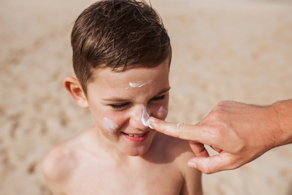 Boy with sunscreen lotion on face. Young boy si protected from sun with sunscreen. Concept of family beach summer vacation with kids.