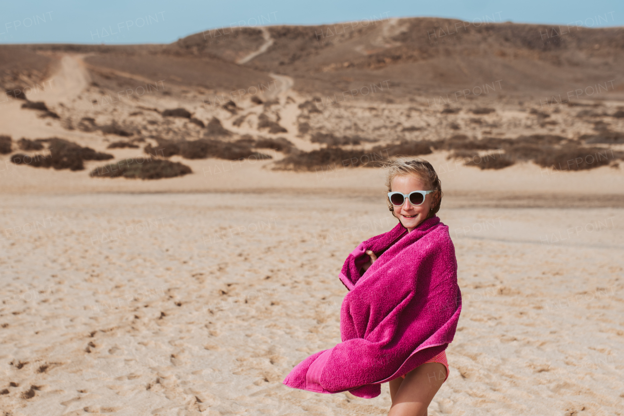 Young girl on beach, wrapped in towel after swim in sea. Concept of family beach summer vacation with kids.