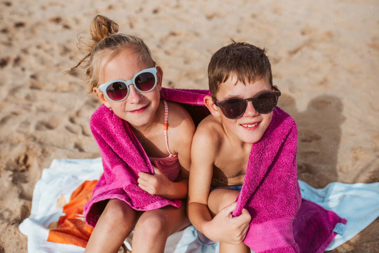 Siblings sitting on beach, wrapped in towel after swim in sea. Concept of family beach summer vacation with kids.