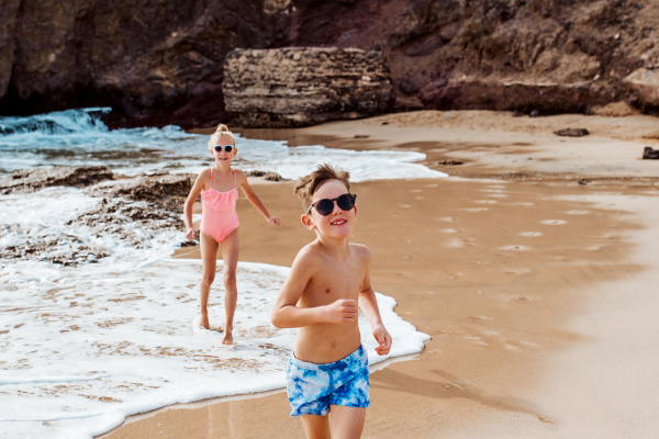 Siblings playing on beach, running, having fun. Smilling girl and boy on sandy beach of Canary islands. Concept of a family beach summer vacation with kids.