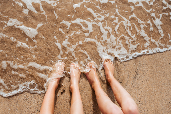 Close up of feet on beach with sea water beneath. Sea foam and warm water soaking legs.