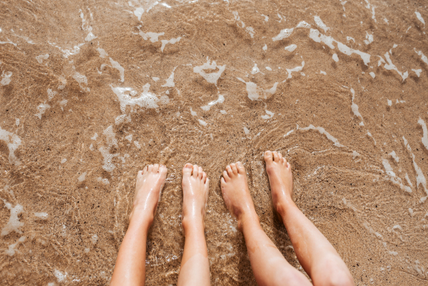 Close up of feet on beach with sea water beneath. Sea foam and warm water soaking legs.