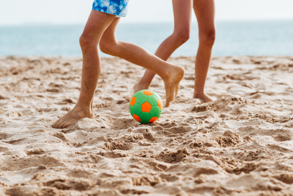 Siblings playing on beach with ball, playing football. Concept of family beach summer vacation with kids. Close up on legs.