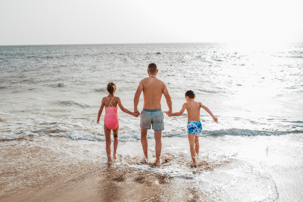 Father with two kids running on beach. Young family enjoying sandy beach, looking at crystalline sea in Canary Islands. Concept of a beach summer vacation with kids.