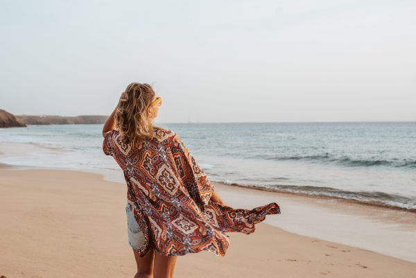 Rear view of a beautiful slim woman standing on sand beach. Full body shot of barefoot woman looking at sea. Concept of beach summer vacation.