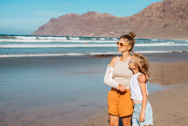 Daughter with mother with broken arm on beach. Arm cast, injured during family vacation in holiday resort. Concept of family beach summer vacation with injury.