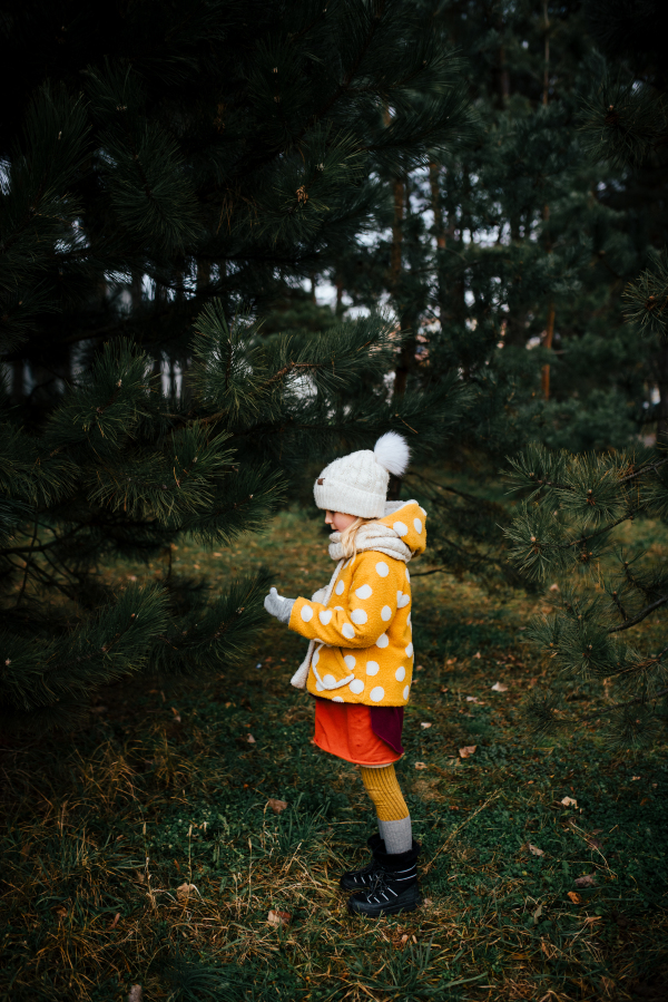 Side view of a little girl standing in the forest, dressed in warm clothing. Spending time outdoors, early spring, autumn season.