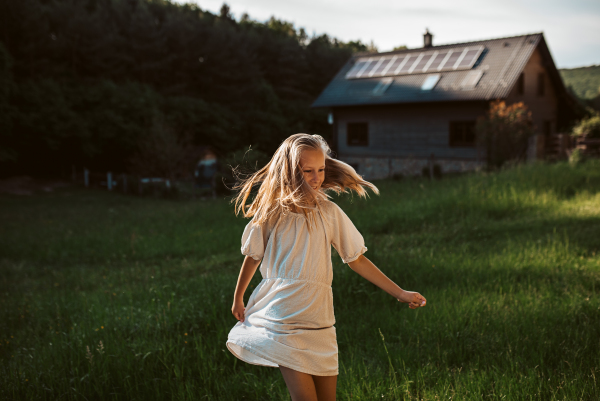 Little girl in front of house with solar panels on roof, jumping, dancing and having fun. Concept of renewable resources, sustainability and green energy.