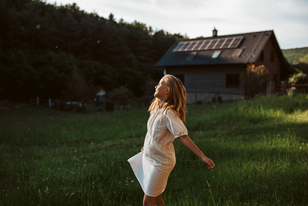 Little girl in front of house with solar panels on roof, jumping, dancing and having fun. Concept of renewable resources, sustainability and green energy.