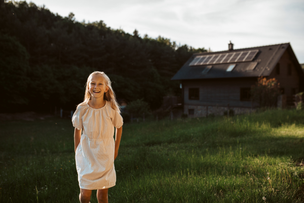 Young girl in front of house with solar panels on roof. Concept of renewable resources, sustainability and green energy.