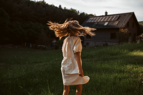 Little girl in front of house with solar panels on roof, jumping, dancing and having fun. Concept of renewable resources, sustainability and green energy.