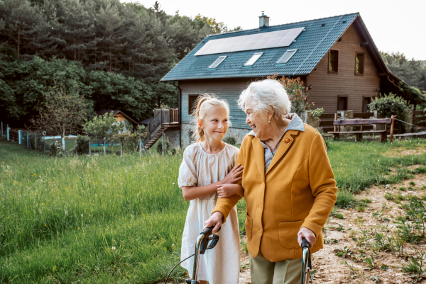 Granddaughter spending time with elderly grandma, companionship. Senior lady with walker on walk with young girl.