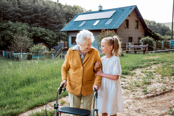 Granddaughter spending time with elderly grandma, companionship. Senior lady with walker on walk with young girl.