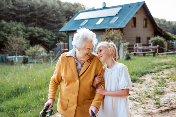 Granddaughter spending time with elderly grandma, companionship. Senior lady with walker on walk with young girl.