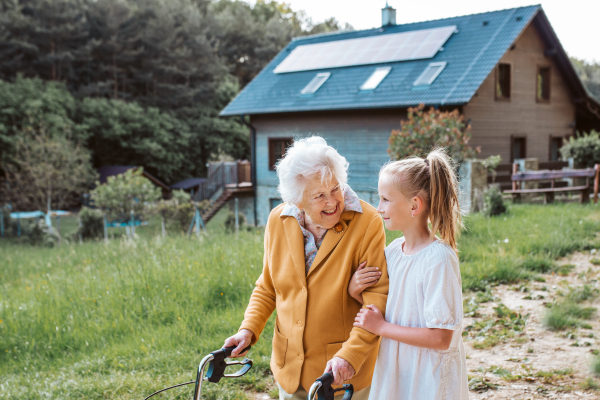 Granddaughter spending time with elderly grandma, companionship. Senior lady with walker on walk with young girl.