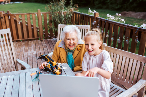 Elderly grandmother supporting granddaughter in robotics, science, IT technologies and programming. Young girl assembling a simple robot and shoving it to grandma.