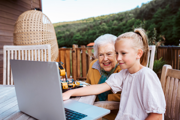 Grandmother supporting granddaughter in robotics, science, IT technologies and programming. Young girl showing her science project on laptop.