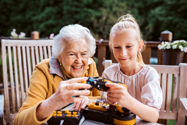 Elderly grandmother supporting granddaughter in robotics, science, IT technologies and programming. Young girl assembling a simple robot and shoving it to grandma.