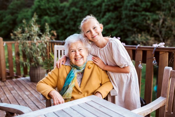 Portrait of granddaughter spending time with elderly grandma, companionship. Senior lady sitting on wooden patio.