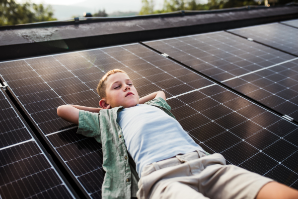 Boy lying on roof with solar panels, eyes closed. Sustainable future for next generation concept.