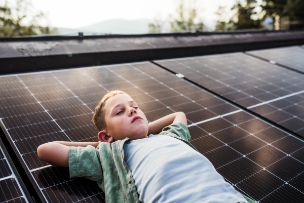 Boy lying on roof with solar panels, eyes closed. Sustainable future for next generation concept.