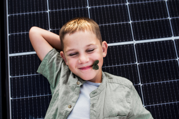 Top view of boy lying on roof with solar panels, looking at camera. Sustainable future for next generation concept.