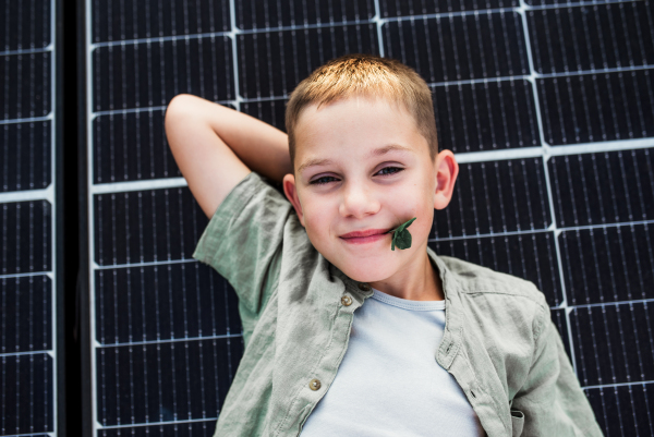 Top view of boy lying on roof with solar panels, looking at camera. Sustainable future for next generation concept.