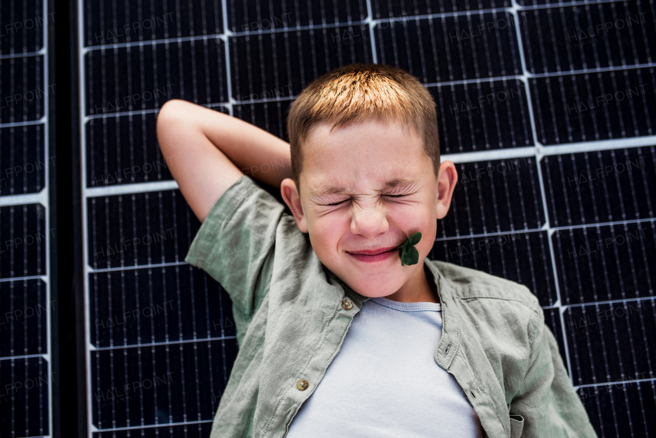 Top view of boy lying on roof with solar panels, looking at camera. Sustainable future for next generation concept.