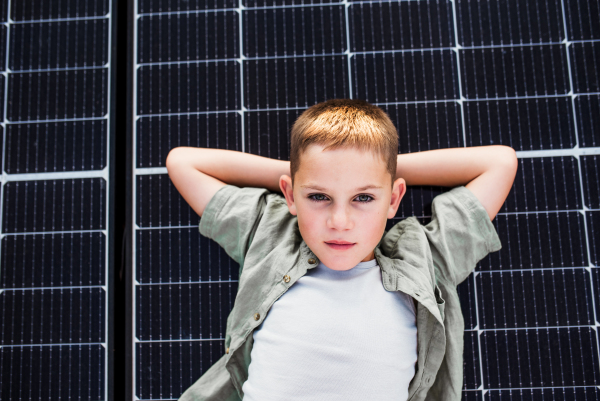 Top view of boy lying on roof with solar panels, looking at camera. Sustainable future for next generation concept.