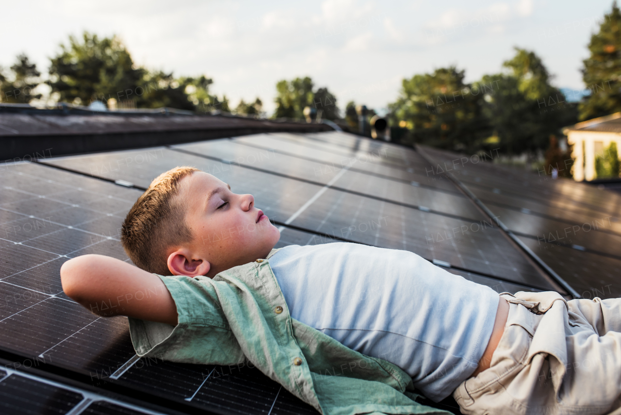 Boy lying on roof with solar panels, eyes closed. Sustainable future for next generation concept.