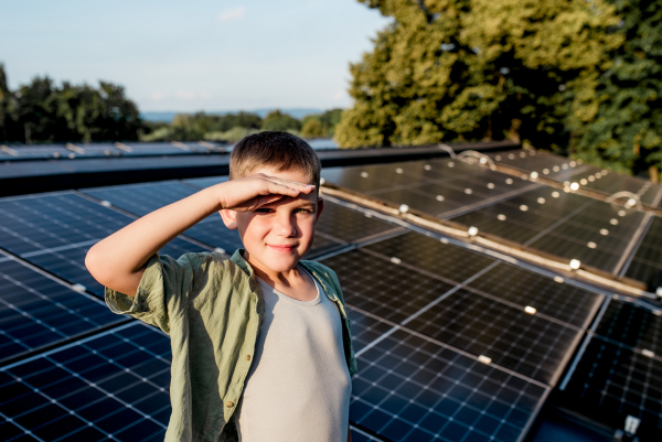 Cute boy on roof with solar panels, hand shielding eyes from summer sun. Sustainable future for next generation concept.