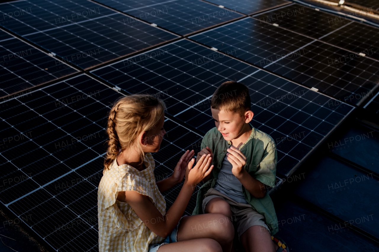 Two young siblings sitting on roof with solar panels, looking at each other.Sustainable future for next generation concept.