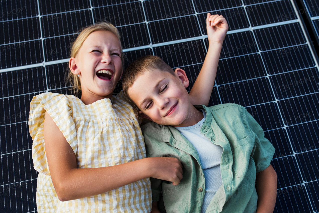 Top view of two young siblings lying on roof with solar panels. Rooftop solar or photovoltaic system. Sustainable future for next generation concept.