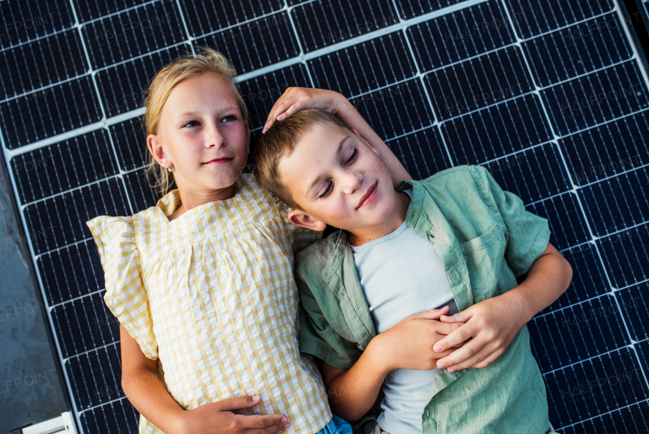 Top view of two young siblings lying on roof with solar panels. Rooftop solar or photovoltaic system. Sustainable future for next generation concept.