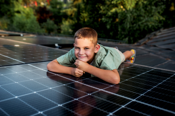 Boy lying on his belly on roof with solar panels, looking at surrounding nature. Sustainable future for next generation concept.