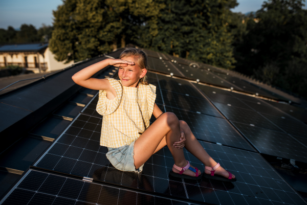 Girl sitting on roof with solar panels during sunset, looking at sunset. Sustainable future for next generation concept.