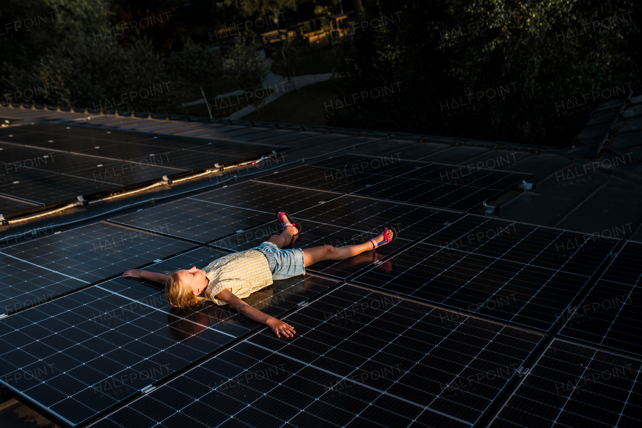 Girl lying on roof with solar panels with closed eyes, enjoying sunset.Sustainable future for next generation concept.