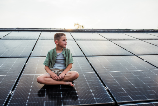 Cute boy sitting on roof with solar panels, looking at surrounding nature. Sustainable future for next generation concept.